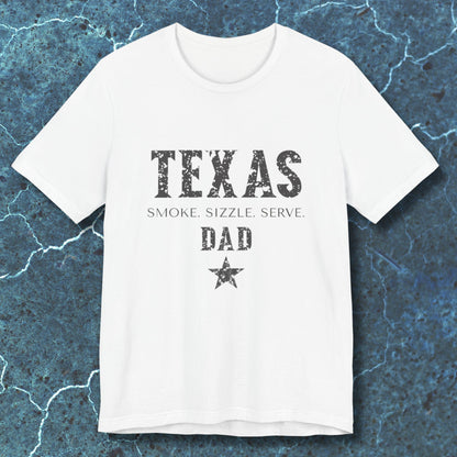 White t-shirt with 'TEXAS SMOKE. SIZZLE. SERVE. DAD' text on a textured blue background