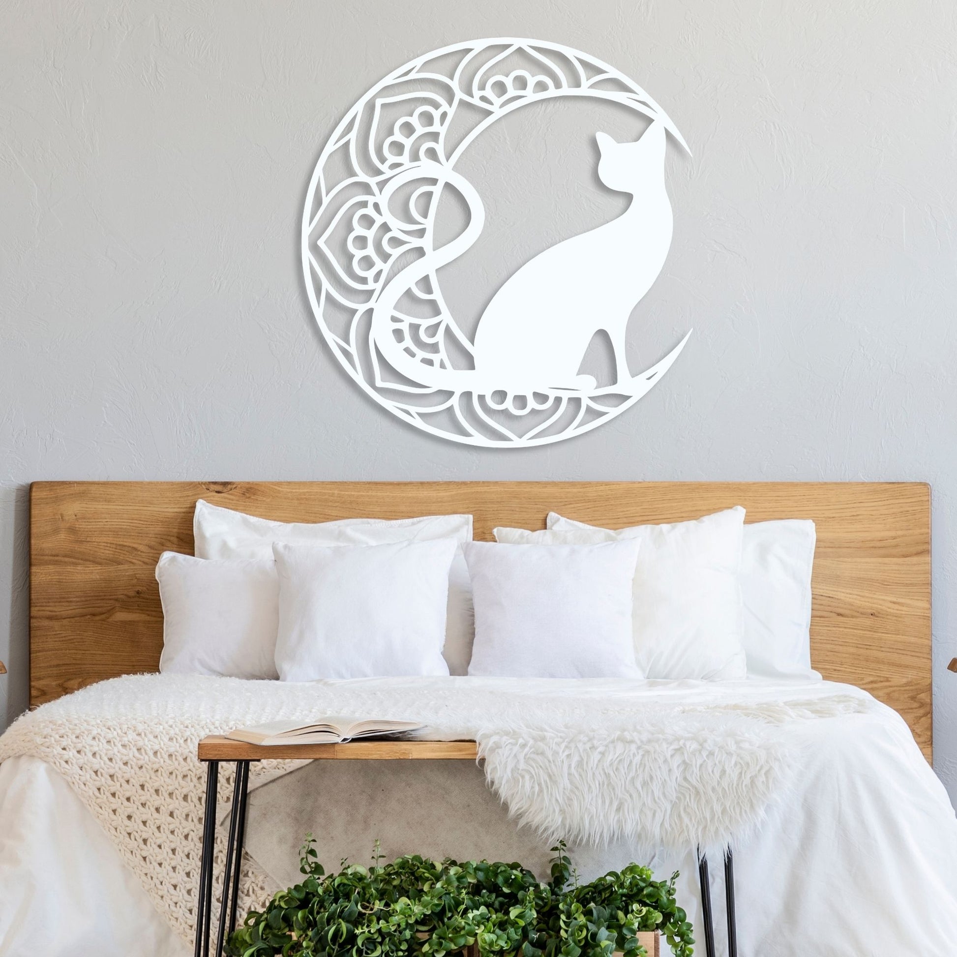 Decorative wall art of a cat in a crescent moon design above a bed with white bedding.