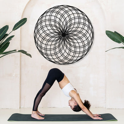 Person in a yoga pose on a mat with a decorative wall piece and plants in the background