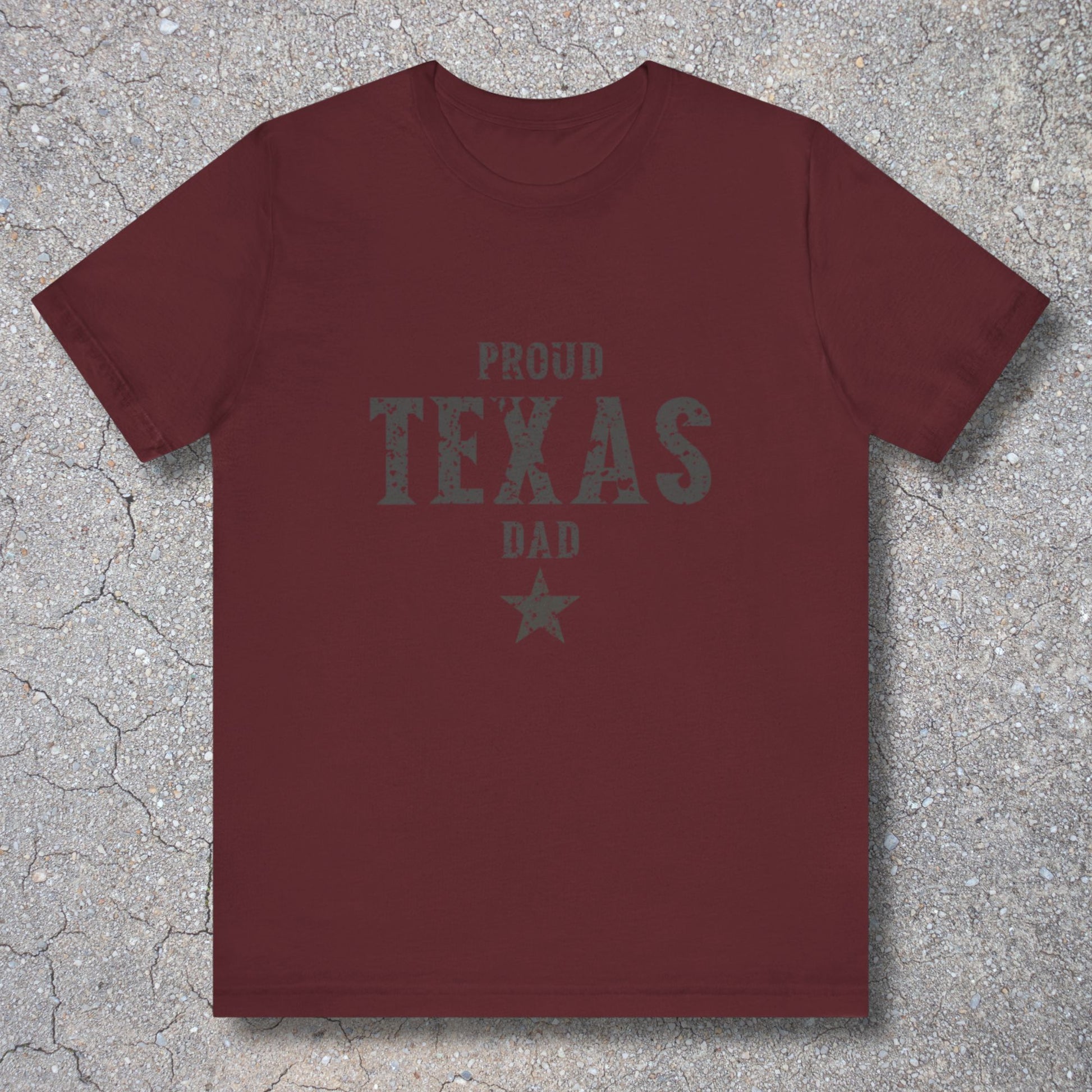 Maroon t-shirt with 'Proud Texas Dad' text on a textured surface