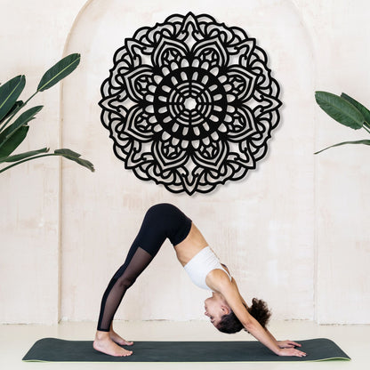 Person practicing yoga in front of a decorative mandala wall art with plants on either side.