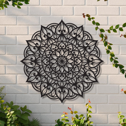 Decorative black mandala wall art on a white brick wall with greenery.