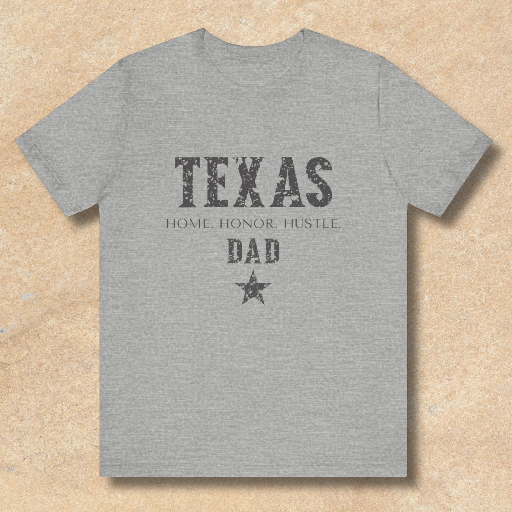 Gray t-shirt with 'Texas Home Honor Hustle Dad' text on a beige background