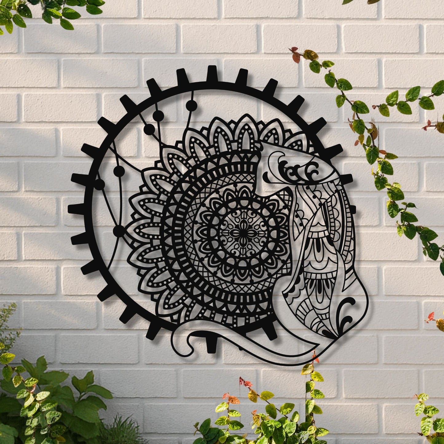 Decorative metal wall art with a fish and mandala design on a white brick wall.