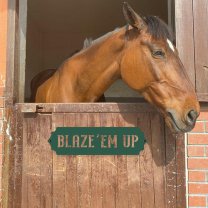 Horse peeking out of a stable with a sign reading 'BLAZE'EM UP'.