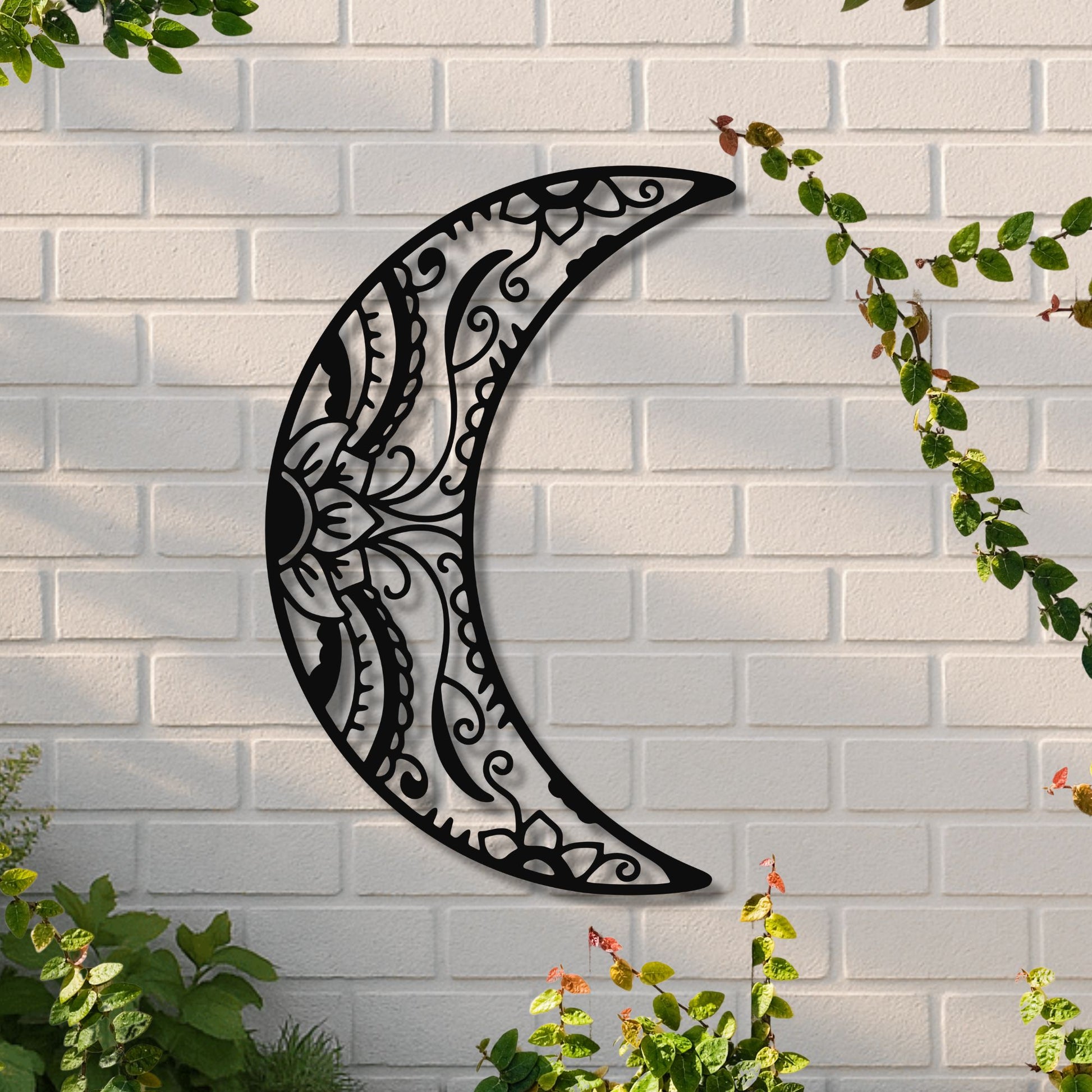 Decorative metal crescent moon wall art on a white brick wall with greenery.