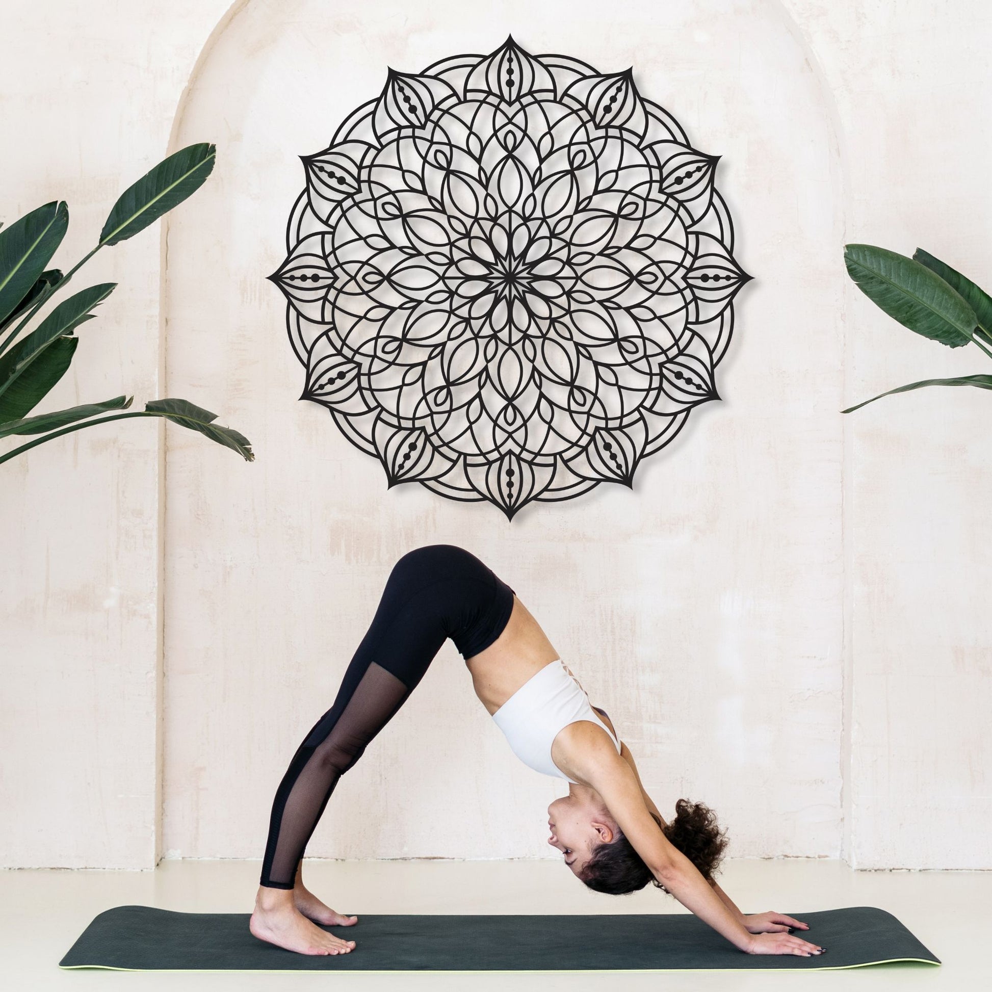 Person practicing yoga in a studio with a decorative wall mandala and plants.