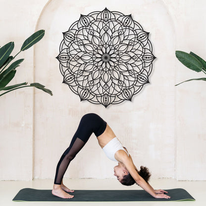 Person practicing yoga in a studio with a decorative wall mandala and plants.