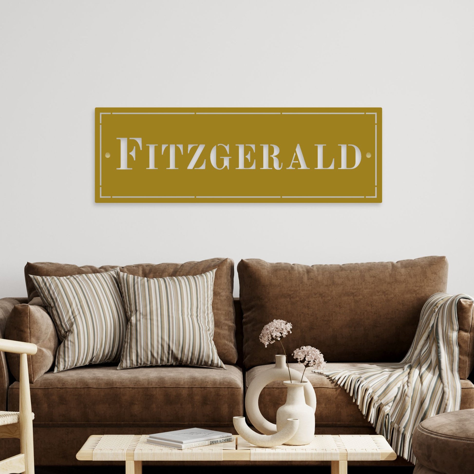 Brown sofa with decorative pillows and a coffee table in a living room setting, featuring a sign with 'Fitzgerald' on the wall.