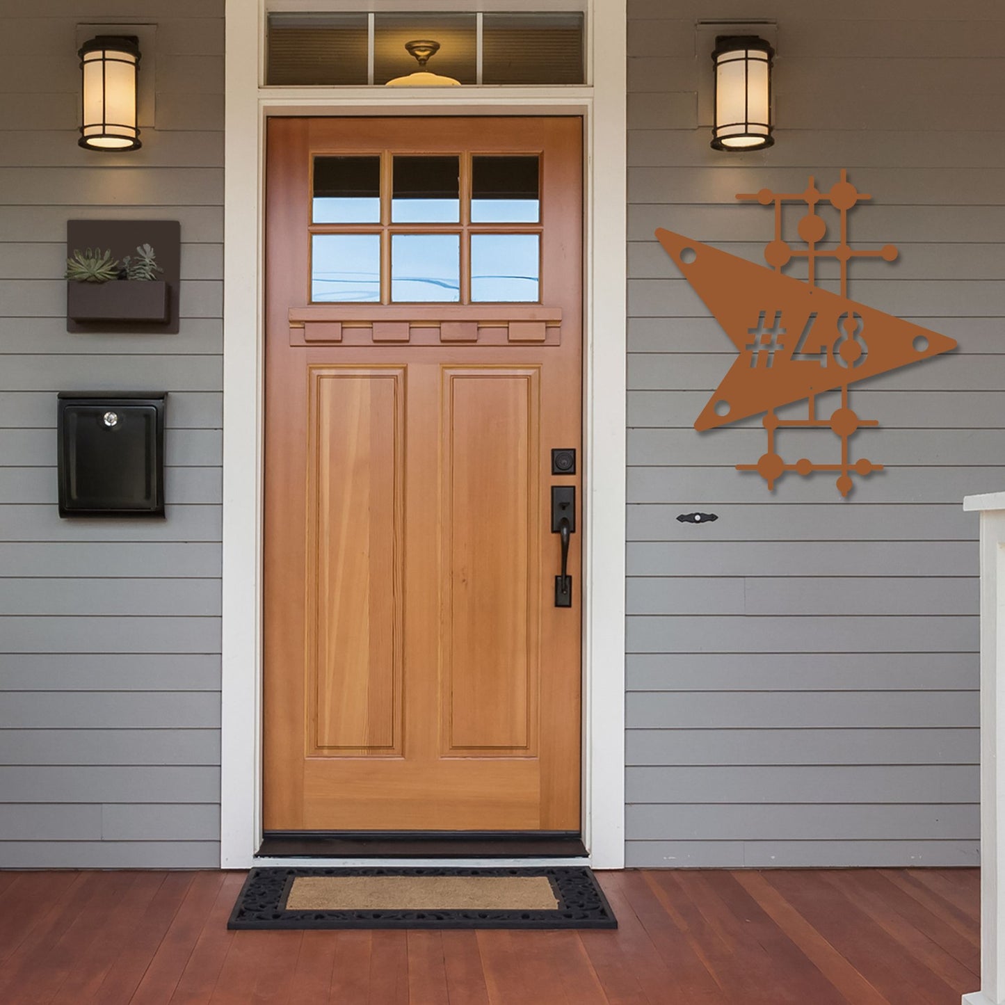 Wooden front door with decorative metal sign on a gray house exterior